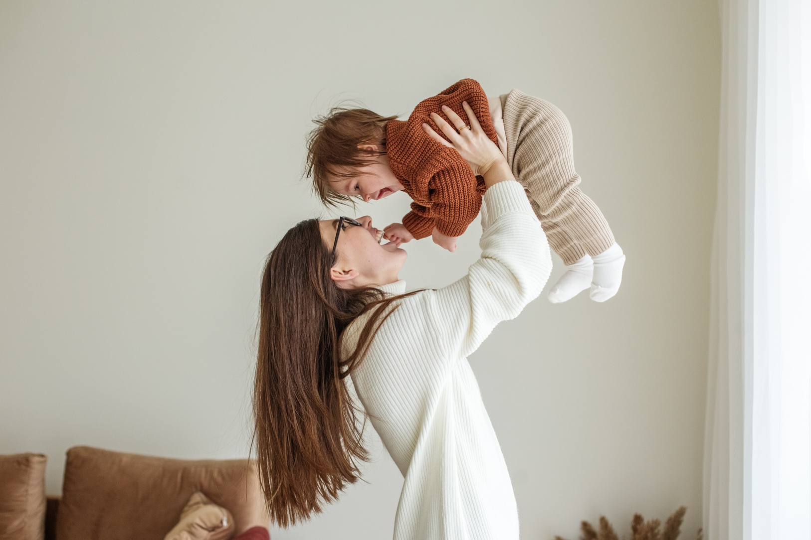 Happy Cheerful Young Mother Throws an Adorable Baby in Air, Plays, Hugs Baby with Love, Care